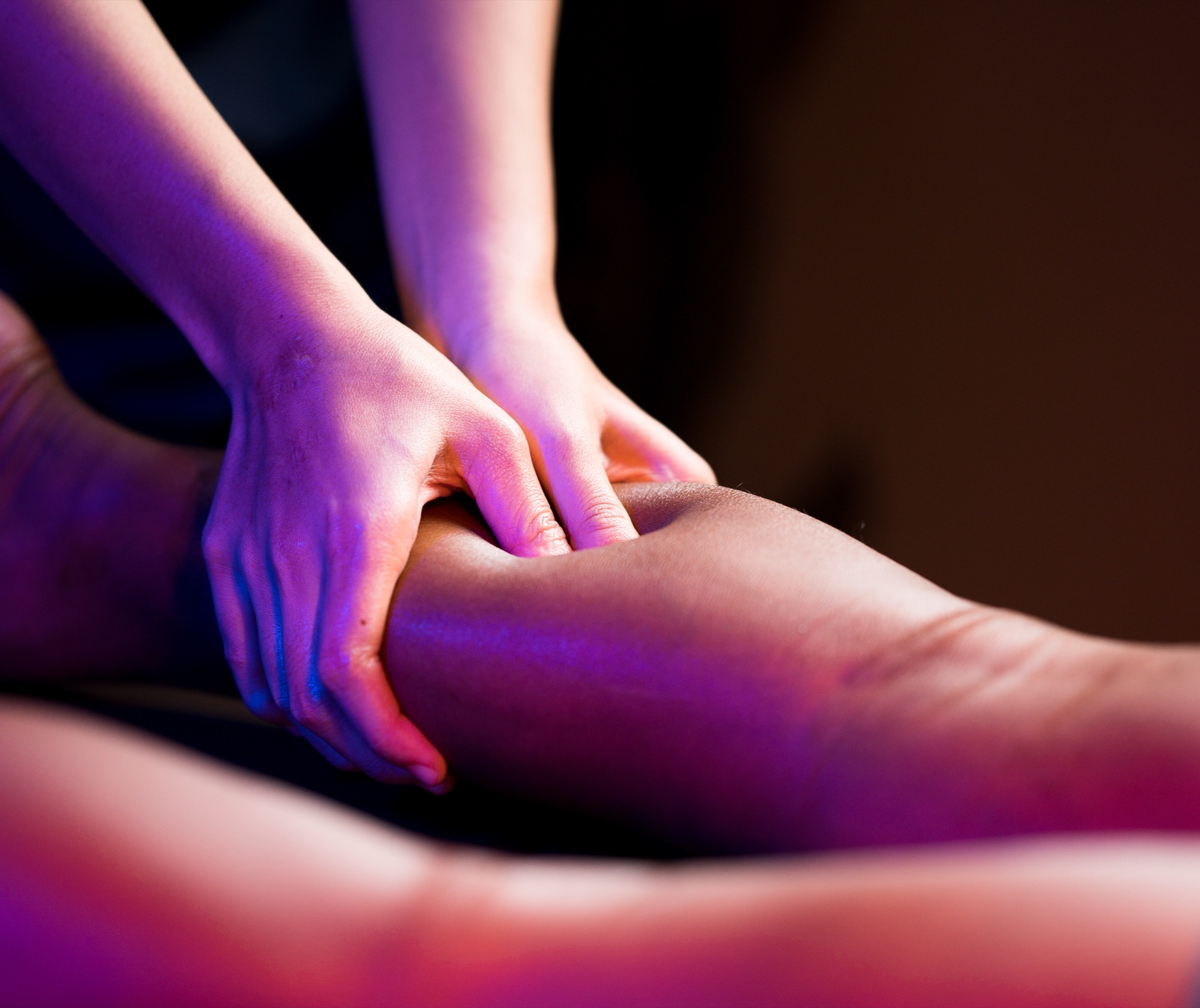 A Bodytune therapist applying sports massage to an athlete's calf under blue and magenta light