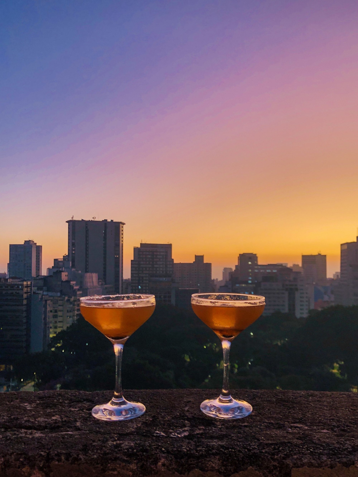 Two cocktails set against a city skyline at sunset