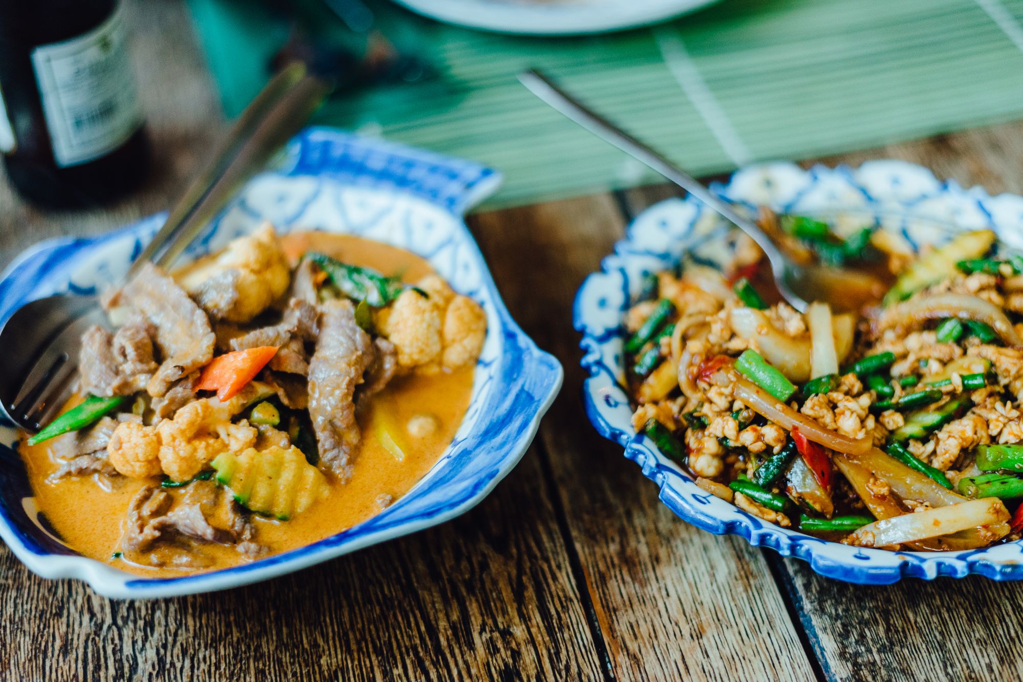 Two Thai dishes served in patterned bowls on a wooden table
