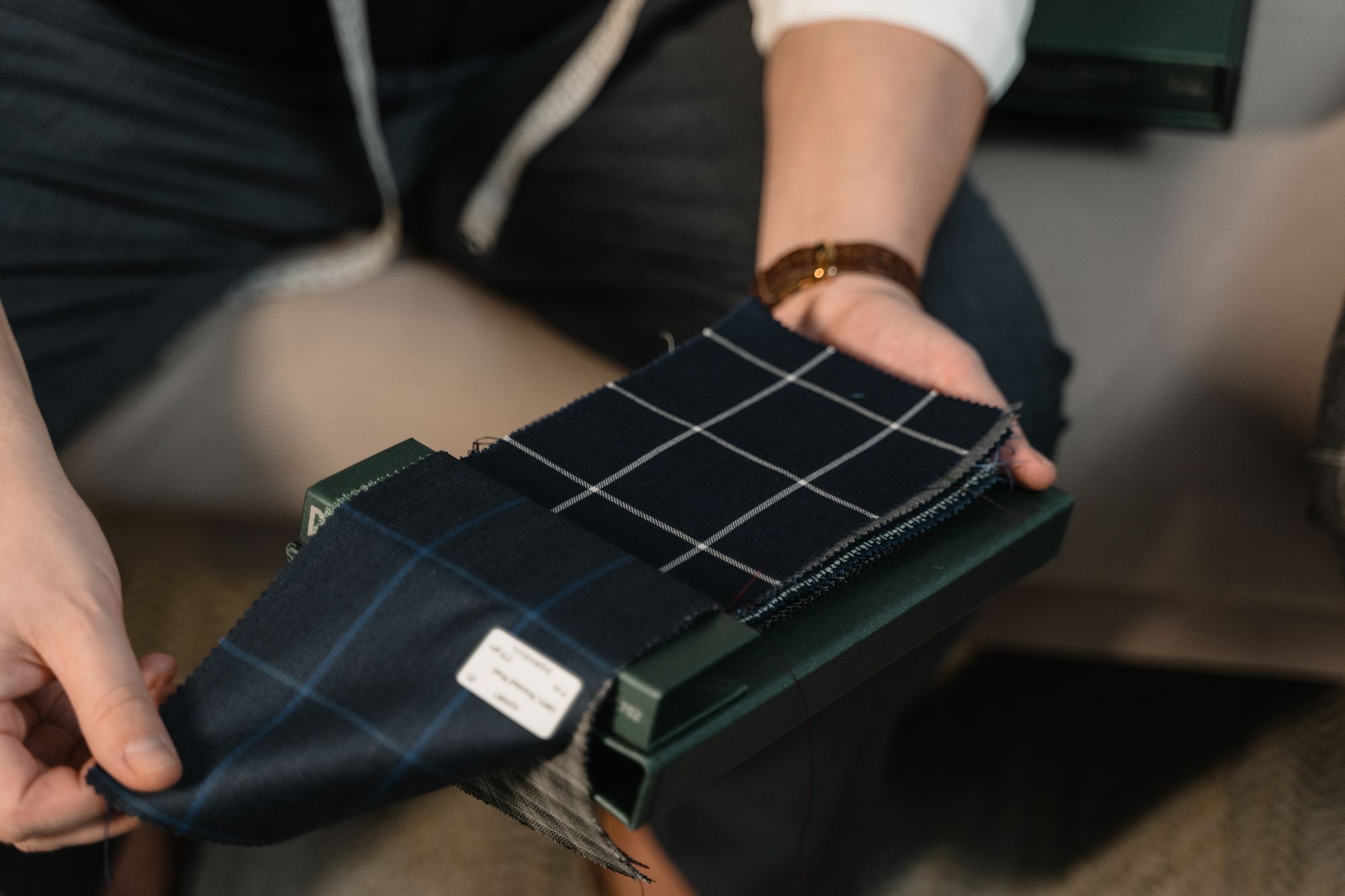 Tailor presenting a stack of dark checked fabric swatches