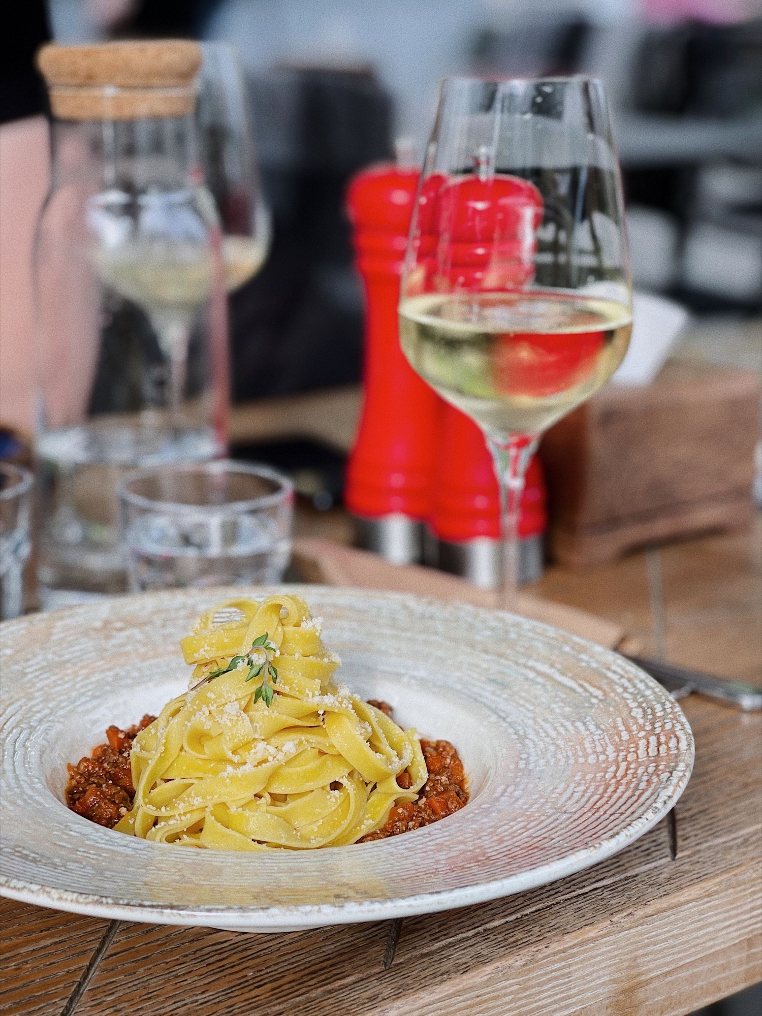 Plate of tagliatelle beside a glass of white wine at a restaurant table