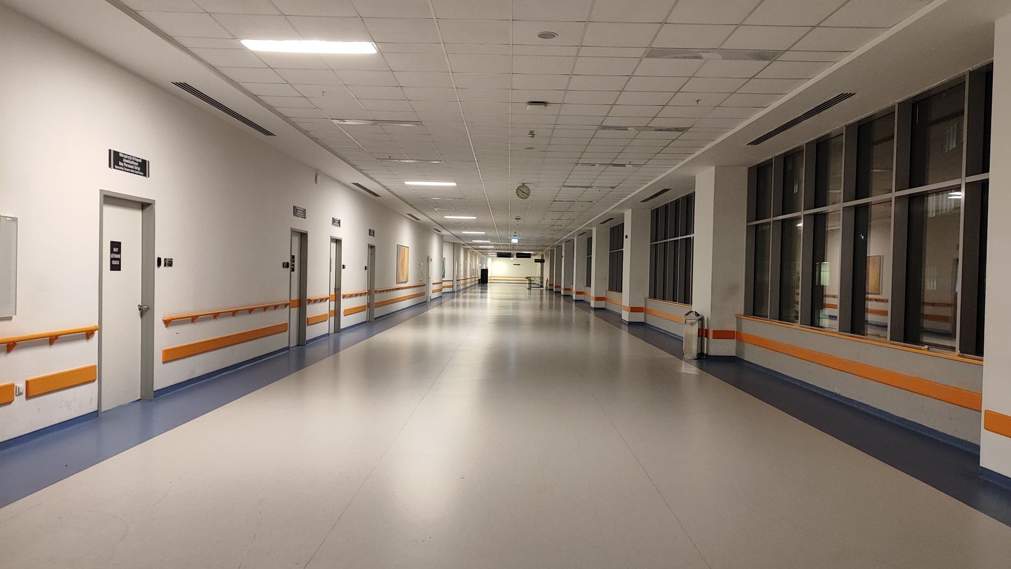 A clean, bright hospital corridor with handrails and treatment-room doors