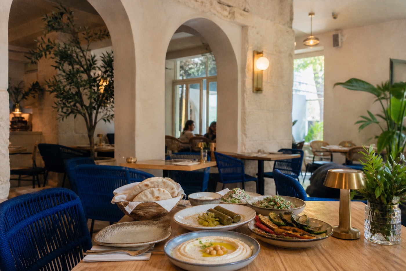 Illustrative Lebanese dining room with pale stone arches, blue chairs and a shared mezze table