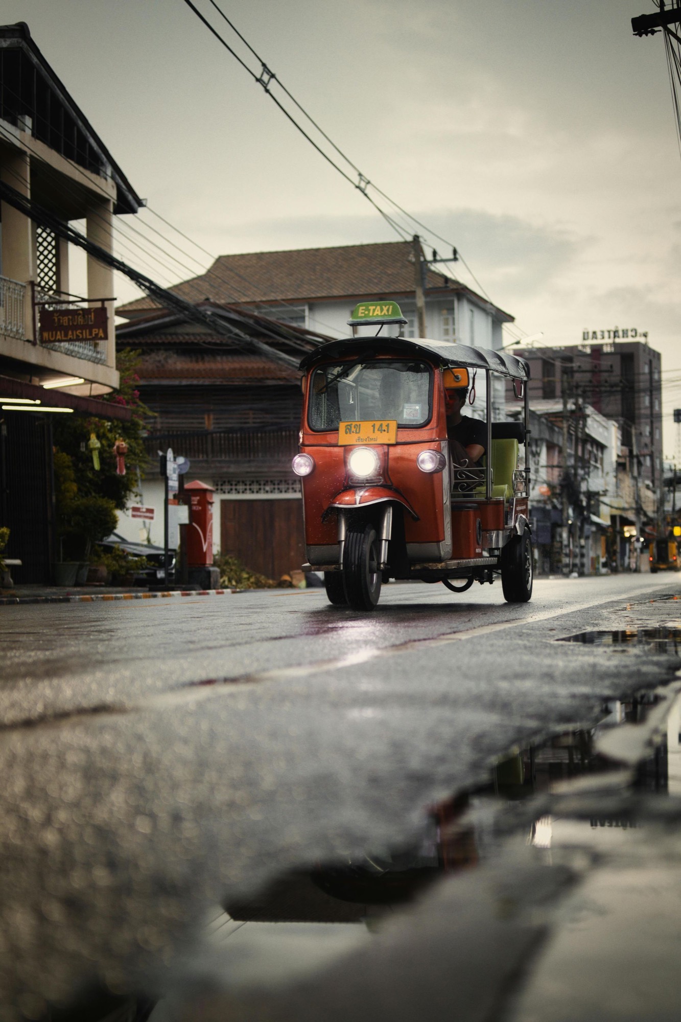 A red tuk-tuk driving along a wet Bangkok street