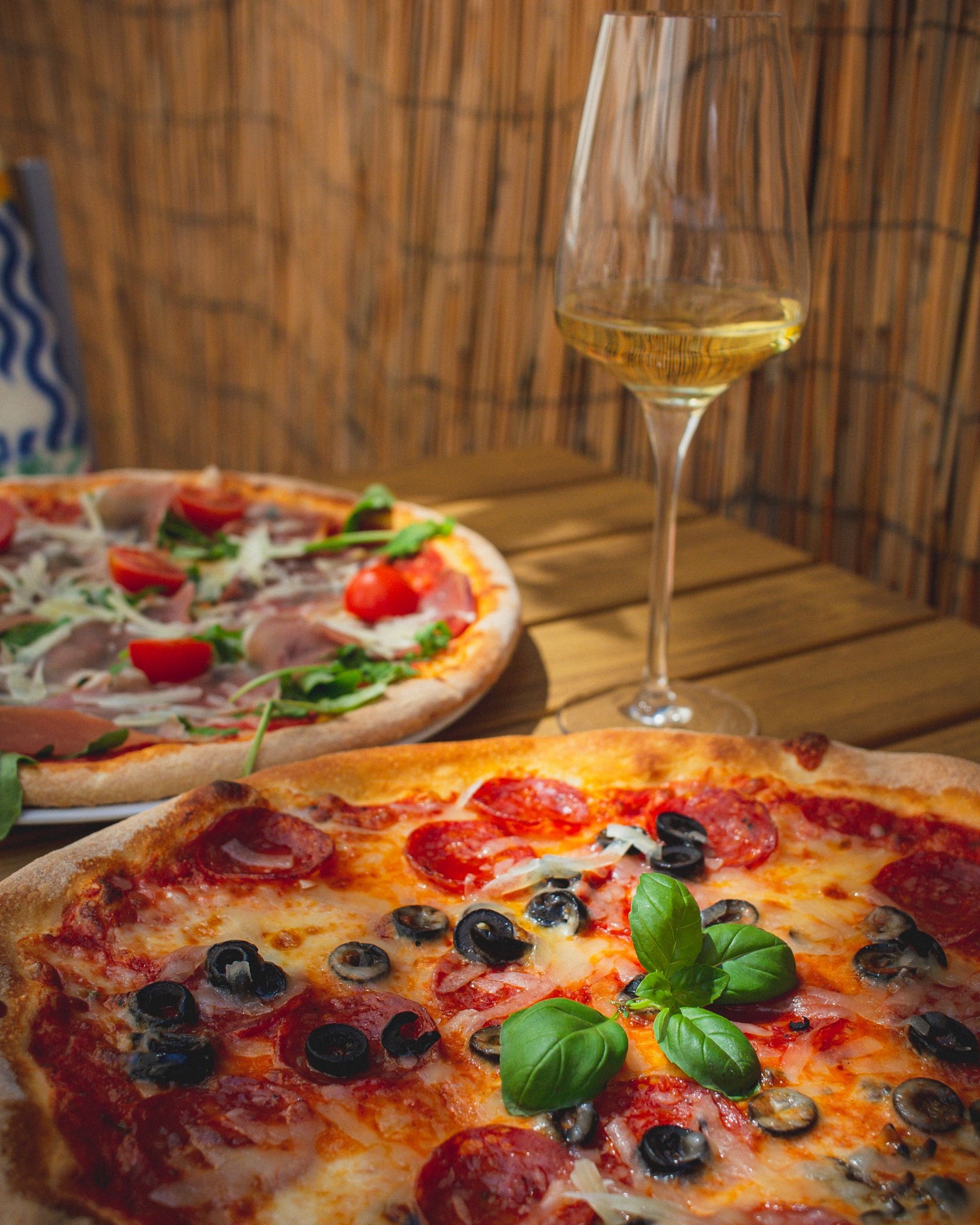 Fresh pizzas and a glass of white wine on a wooden restaurant table